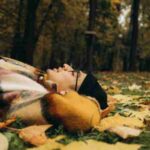 A man in a colorful coat lies peacefully among fall leaves in a serene forest setting., tags: zwischen und - pexel